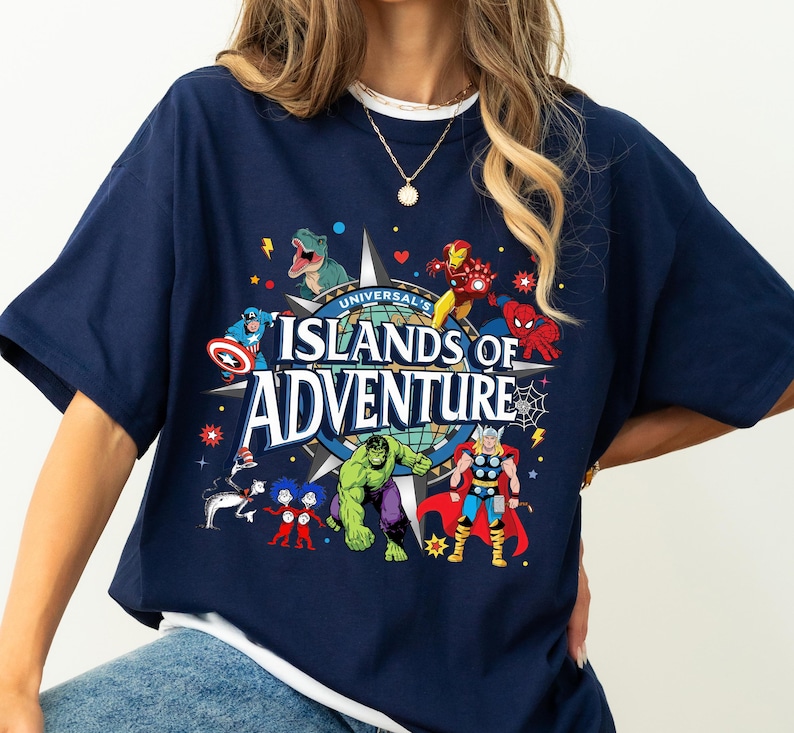 May include: Navy blue t-shirt featuring a colorful graphic of various Marvel characters and the text "Universal's Islands of Adventure." The design includes Iron Man, Spider-Man, Hulk, and Thor. The shirt has short sleeves and a crew neck.