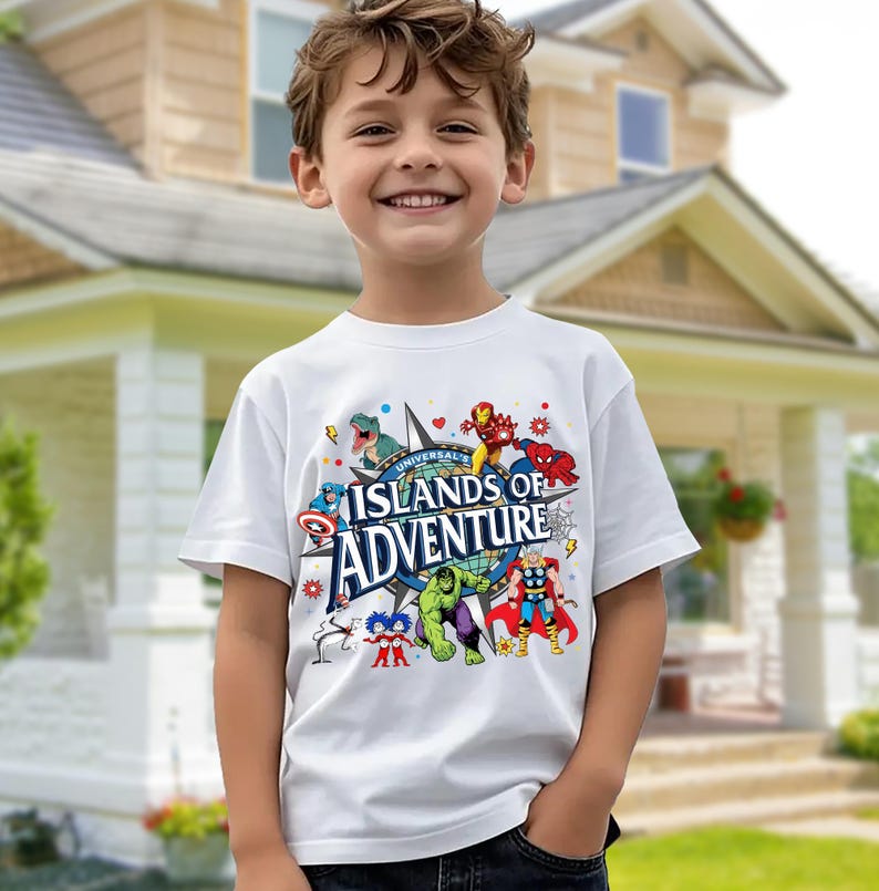 May include: A white t-shirt featuring the text "UNIVERSAL ISLANDS OF ADVENTURE" in a blue and white design. The shirt is decorated with colorful cartoon characters, including superheroes and a dinosaur.
