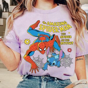 May include: A light purple t-shirt featuring a graphic of Spider-Man and Stitch. The text reads "The Amazing Spider-Man" and "The Spider or the Stitch?" in yellow and white. The design includes a spider web and star accents.