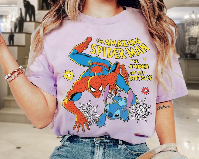 May include: A light purple t-shirt featuring a graphic of Spider-Man and Stitch. The text reads "The Amazing Spider-Man" and "The Spider or the Stitch?" in yellow and white. The design includes a spider web and star accents.