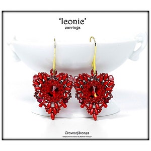 Può includere: Un paio di orecchini rossi a forma di cuore con ganci color oro. Gli orecchini sono fatti di piccole perline rosse e gemme rosse più grandi. La parola "Iconic" è nella parte superiore dell'immagine, e le parole "Crown of Stones" sono nella parte inferiore.
