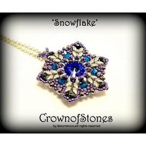 以下が含まれることがあります： 銀色のチェーンネックレスと雪の結晶ペンダント。ペンダントは、中央に大きな青いクリスタルがあり、その周りに小さな青と銀の要素があります。画像には「Snowflake」と「CrownofStones」という文字が含まれています。