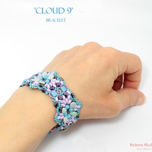 May include: A beaded bracelet with the text "CLOUD 9" and "BRACELET". The bracelet features a floral design with light blue, lavender, and dark purple beads. The bracelet is worn on a wrist.