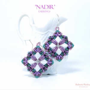 May include: A pair of handcrafted earrings with a geometric design. The earrings feature a square shape with a white center and are adorned with purple, teal, and black beads. The text "NADIR" and "EARNINGS" is visible.