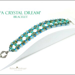 Può includere: Un braccialetto di perline con il testo "A Crystal Dream" e "Bracelet". Il braccialetto presenta un motivo di perline turchesi e blu con accenti dorati. Ha una chiusura color argento.