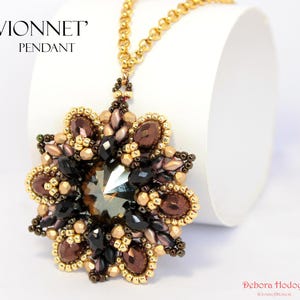 Può includere: Una collana dorata con un grande pendente. Il pendente a forma di fiore presenta una pietra centrale sfaccettata, circondata da pietre marroni e nere e perline dorate. Il testo "VIONNET PENDANT" è in alto a sinistra.