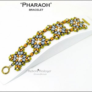 May include: A beaded bracelet with the word "PHARAOH" above the word "BRACELET". The bracelet features a repeating floral design in shades of gold, gray, and green, with a gold clasp and ring. The bracelet is displayed on a white surface.