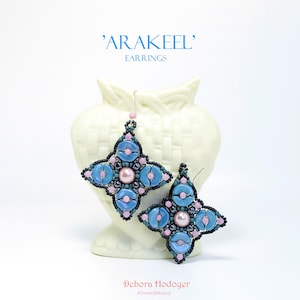 Peut inclure: Paire de boucles d'oreilles 'Arakeel' faites à la main. Chaque boucle d'oreille présente un motif à quatre pétales avec des perles bleu clair et roses, une perle centrale et des accents noirs. Le texte 'Arakeel' et 'Earrings' sont visibles.