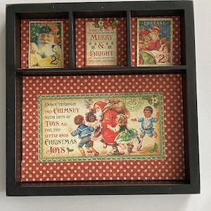 May include: A black wooden display box with four compartments, each featuring vintage Christmas-themed images. The images include Santa Claus, children, and holiday greetings. The background is a red and white patterned paper.