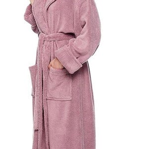 May include: A mauve hooded bathrobe with a matching belt and two front pockets. The plush robe is made of a soft material and has long sleeves. The model is wearing the robe and standing on a white background.