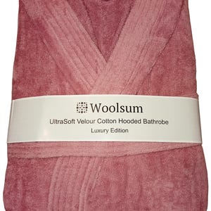 May include: A folded, dusty rose-colored hooded bathrobe. The bathrobe is wrapped with a white band that reads "Woolsium UltraSoft Velour Cotton Hooded Bathrobe Luxury Edition."