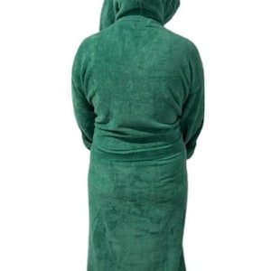 May include: A hooded, emerald green terry cloth robe. The robe has long sleeves and a belt at the waist. The person is facing away from the camera. The robe is made of a soft, absorbent material, perfect for after a shower or a relaxing day.