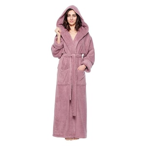 May include: A full-length, hooded, mauve-coloured terry cloth robe with a matching belt and pockets. The robe is made of a soft, plush material, ideal for lounging. The model is wearing the robe.