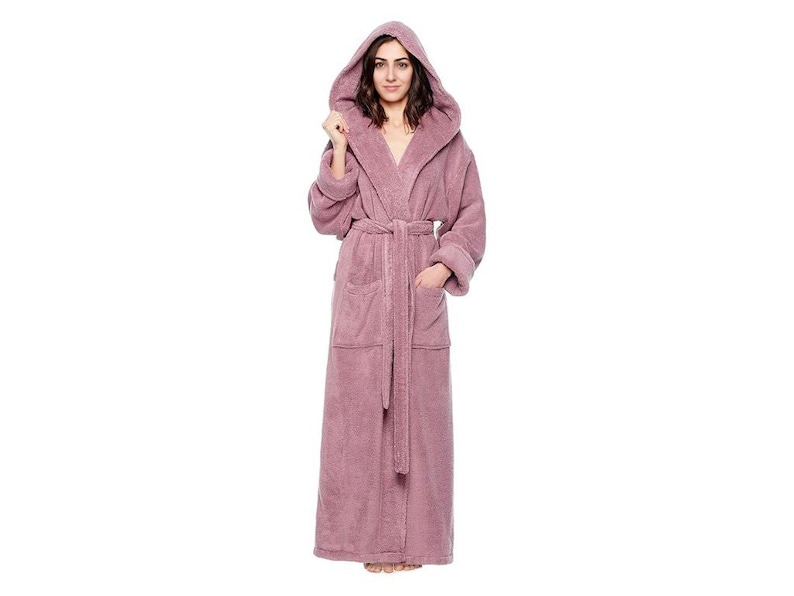 May include: A full-length, hooded, mauve-colored terry cloth robe with a matching belt and pockets. The robe is made of a soft, plush material, perfect for lounging. The model is wearing the robe.