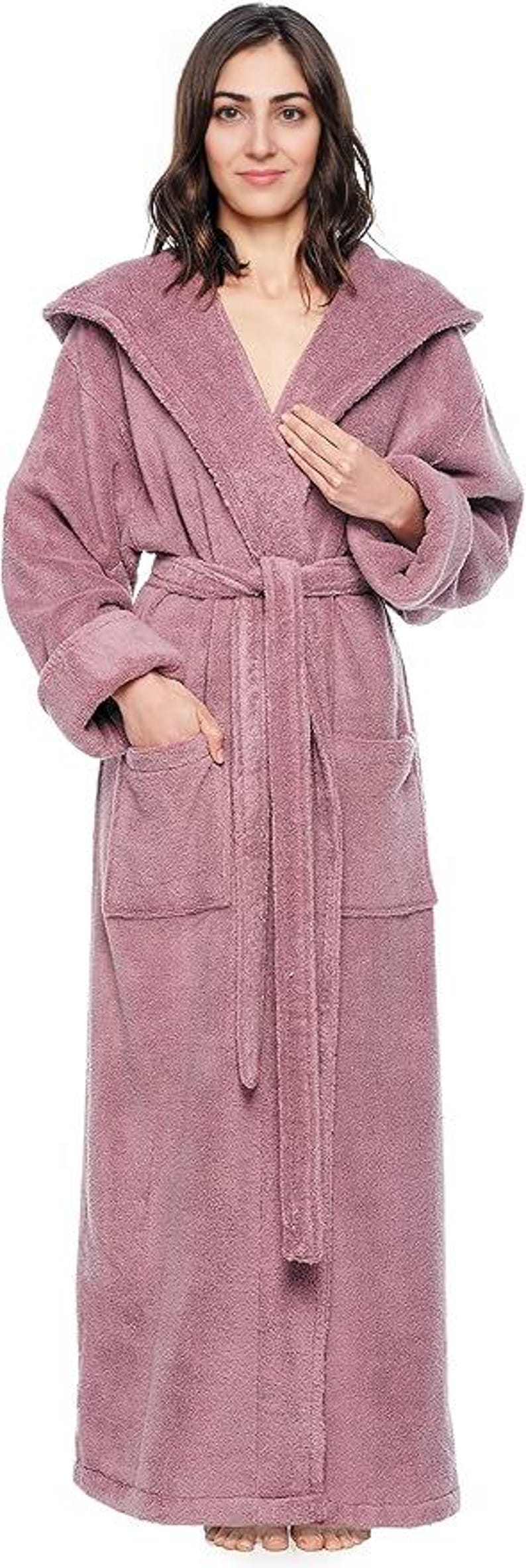 May include: A long, dusty rose-colored hooded robe with a matching belt and pockets. The robe is made of a soft, plush material, perfect for lounging. The model is wearing the robe.