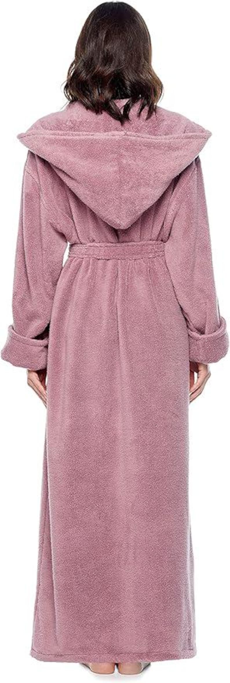 May include: A long, dusty rose-colored hooded robe with a matching belt. The robe has long sleeves with folded cuffs. The model is wearing the robe, standing with their back to the camera.