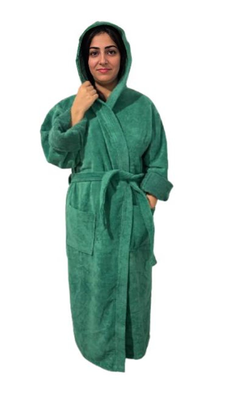 May include: A hooded, emerald green terry cloth robe with a matching belt and pockets. The robe is knee-length and has long sleeves with folded cuffs. The model is wearing the robe.