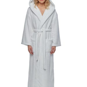 May include: A full-length white hooded bathrobe with a matching belt and pockets. The robe is made of a soft, plush material. The model is wearing the robe.