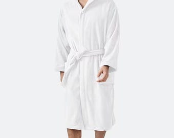 May include: A white hooded bathrobe with a matching belt. The robe has long sleeves and pockets. The model is wearing the robe. The robe is made of a soft, plush material.