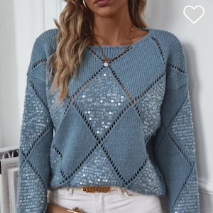 May include: A light blue knit sweater with a diamond pattern and sequin accents. The sweater has long sleeves and a round neckline. A gold-colored belt and a tan purse are also visible.