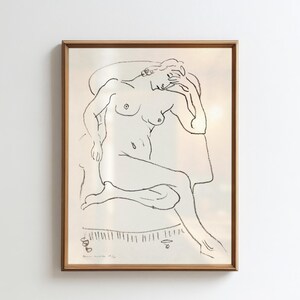 May include: A framed black and white line drawing of a nude figure seated in a chair. The artwork features a minimalist style with delicate lines and shading. The frame is a warm brown color, adding a classic touch to the piece.