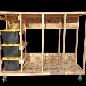 Könnte beinhalten: Ein Holz-Aufbewahrungseinheit auf Rädern mit drei schwarzen Behältern mit gelben Deckeln auf der linken Seite. Die Einheit besteht aus unbehandeltem Holz und Spanplatten. Die Einheit hat ein offenes Design mit vertikalen Stützen.
