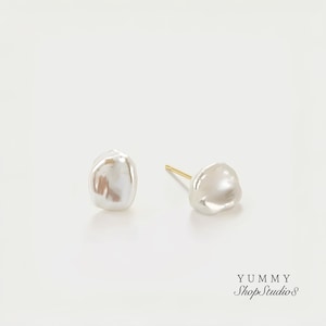 Può includere: Un paio di orecchini a lobo con perle bianche di forma irregolare con perni dorati. Gli orecchini hanno una superficie liscia e lucida su uno sfondo bianco. Un gioiello classico.