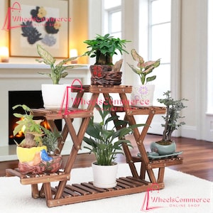 May include: A multi-tiered, wooden plant stand with several potted plants. The stand is made of dark brown wood and has a triangular design. The plants are in various pots, including white, ceramic, and decorative containers. The background includes a fireplace and artwork.