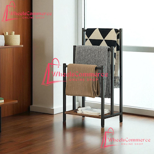 May include: A black metal blanket rack with a wooden shelf. Three blankets in neutral colors are draped over the rack. The blankets are beige, gray, and black and white patterned. The rack is in front of a window.
