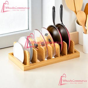 May include: A bamboo kitchen organizer holds plates, lids, and pans. The organizer has multiple slots to separate items. The pans are black with red interiors. The image also shows wooden cooking utensils.