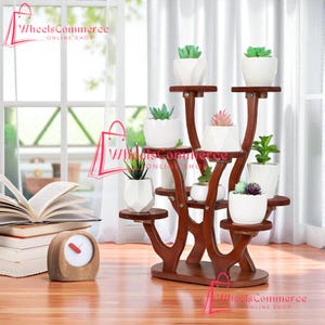 May include: A multi-tiered, dark wood plant stand displaying several small potted succulents. The stand has a unique, curved design with multiple shelves. The white ceramic pots hold various green and pink succulents. The background includes a window and a stack of books.