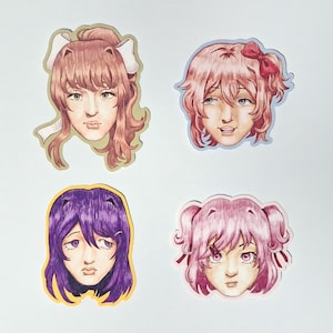 Peut inclure: Quatre autocollants découpés représentant des portraits de personnages inspirés de l'anime. En haut à gauche, un personnage aux cheveux bruns avec un nœud blanc, en haut à droite un personnage aux cheveux roses avec un nœud rouge, en bas à gauche un personnage aux cheveux violets, et en bas à droite un personnage aux cheveux roses avec des couettes.