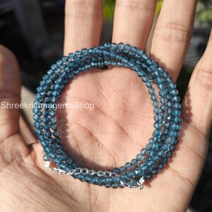 Könnte beinhalten: Mehrreihige Halskette aus kleinen, facettierten blauen Perlen. Die Halskette hat einen silberfarbenen Verschluss und eine Kette. Der Text "ShreekrishnagemsShop" ist im Bild zu sehen.