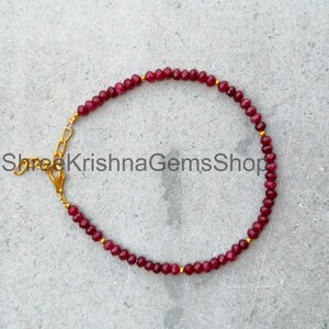 May include: A beaded bracelet featuring small, faceted, deep red ruby beads arranged in a circular pattern, accented with tiny gold-toned metal spacers and a gold-toned lobster claw clasp with an adjustable chain extension.