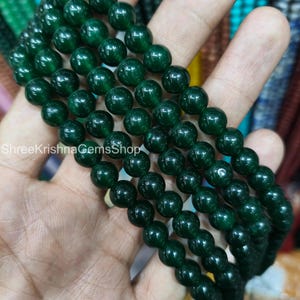 May include: Close-up of multiple strands of dark green gemstone beads. The beads are spherical and have a polished, glossy surface. The text "ShreeKrishnaGemsShop" is visible. These beads are suitable for crafting jewellery.