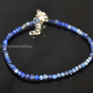 May include: A delicate bracelet featuring small, faceted blue lapis lazuli beads. The bracelet has a silver-colored clasp and chain. The beads are a deep blue color with some lighter, speckled variations.