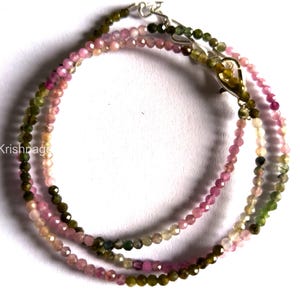 May include: Three delicate gemstone necklaces. The necklaces are made of small, round beads in shades of pink, green, and brown. The necklaces are connected with silver clasps. The background is white.