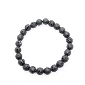 Puede incluir: Una pulsera de cuentas de piedra de lava negra. La pulsera presenta cuentas redondas y porosas ensartadas en una banda elástica. Las cuentas son de color carbón oscuro y la pulsera se muestra sobre un fondo blanco. La letra "S" es visible en una de las cuentas.