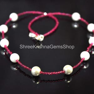Könnte beinhalten: Halskette mit großen, weißen Perlen, abwechselnd mit kleinen, roten Perlen. Die Kette ist auf einem roten Band aufgefädelt und hat einen silbernen Verschluss. Der Text "ShreeKrishnaGemsShop" ist sichtbar.