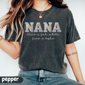 Peut inclure: T-shirt gris fonc&eacute; avec le mot "NANA" dans un motif patchwork. En dessous, les noms Alexis, Joah, Bella, James et Sophia sont imprim&eacute;s. Le t-shirt est de style col rond.