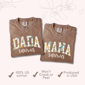 May include: Two brown t-shirts with the words "DADA saurus" and "MAMA saurus" in a white, dinosaur-themed font. The shirts are made of 100% US cotton and produced in the USA.