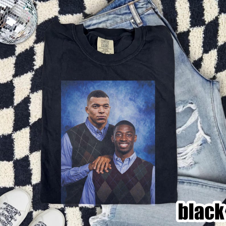 May include: A black crew neck t-shirt featuring a graphic print of two men wearing light blue button-down shirts and dark argyle sweater vests against a blue mottled background. The shirt has a Comfort Colors brand label at the inner neckline.