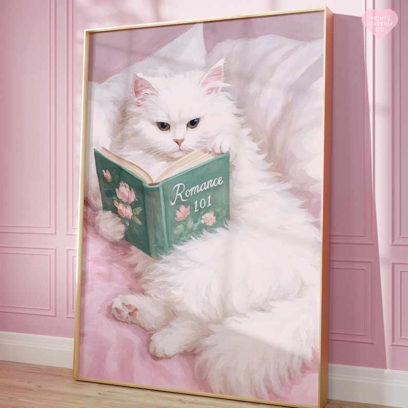 May include: A framed print featuring a fluffy white cat lounging on a pink surface, reading a book titled "Romance 101." The book has a teal cover with floral accents. The artwork is set in a gold frame.