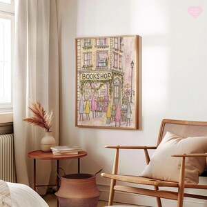 May include: Watercolor print of a bookstore with the word "BOOKSHOP" above the entrance. The artwork features a building with windows, a green awning, and figures in colorful coats. The print is framed in a light wood frame.