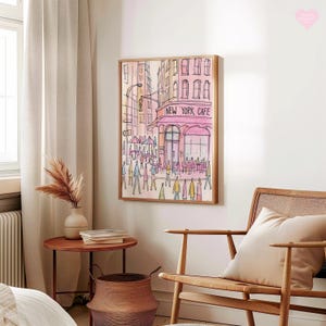 May include: Watercolor painting of a New York City street scene, framed in light wood. The artwork depicts a cafe with the text "NEW YORK CAFE" in pink, surrounded by pedestrians and buildings in shades of pink and orange. The style is illustrative.