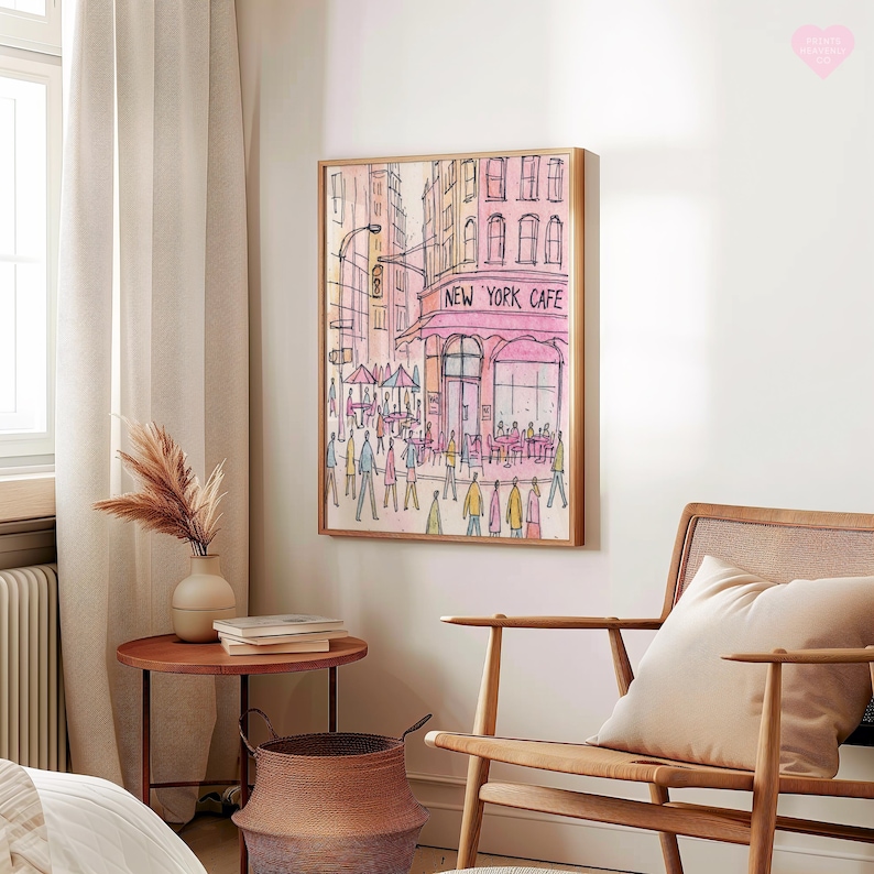 May include: Watercolor painting of a New York City street scene, framed in light wood. The artwork depicts a cafe with the text "NEW YORK CAFE" in pink, surrounded by pedestrians and buildings in shades of pink and orange. The style is illustrative.