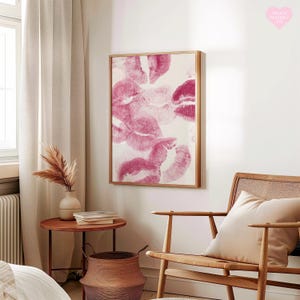 May include: A framed artwork featuring multiple pink lipstick kiss prints on a white background. The artwork is displayed in a room with a wooden chair, a side table, and a woven basket. The overall theme is home decor.