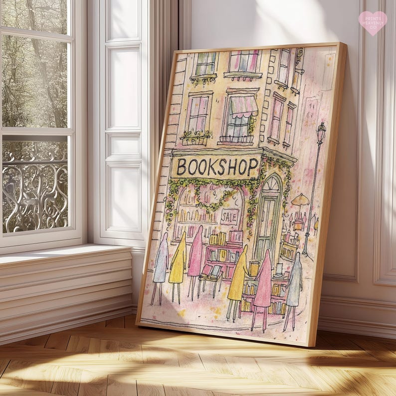 May include: Watercolor print of a bookshop with the word "BOOKSHOP" above the entrance. The artwork features a building with windows, awnings, and a sale sign. Figures in yellow, pink, and gray coats stand in front of the shop. The print is in a wooden frame.