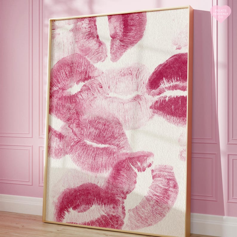 May include: A framed art print featuring multiple lip imprints in varying shades of pink and magenta against a white background. The artwork is displayed in a gold-colored frame, creating a romantic and artistic aesthetic.