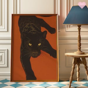 May include: A framed art print of a black panther against an orange backdrop. The panther has yellow eyes and is in a dynamic pose. The gold-coloured frame enhances the artwork. The print is displayed indoors, adding a touch of sophistication to the space.